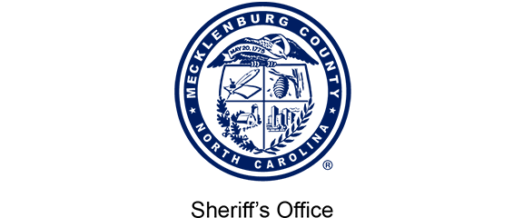 Seal of Mecklenburg County, North Carolina with various symbols, surrounded by text reading “Mecklenburg County North Carolina.” Text below reads “Sheriff’s Office.”.
